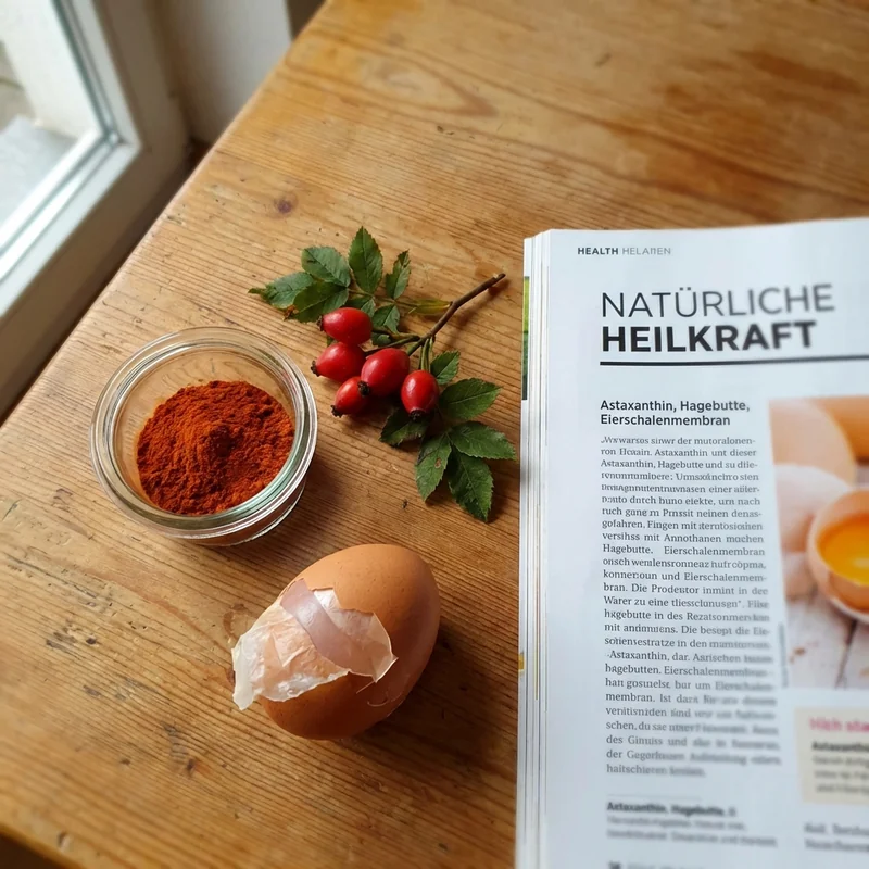 Naturstoffe: Astaxanthin-Pulver, Hagebutten, Eierschalenmembran auf Holztisch