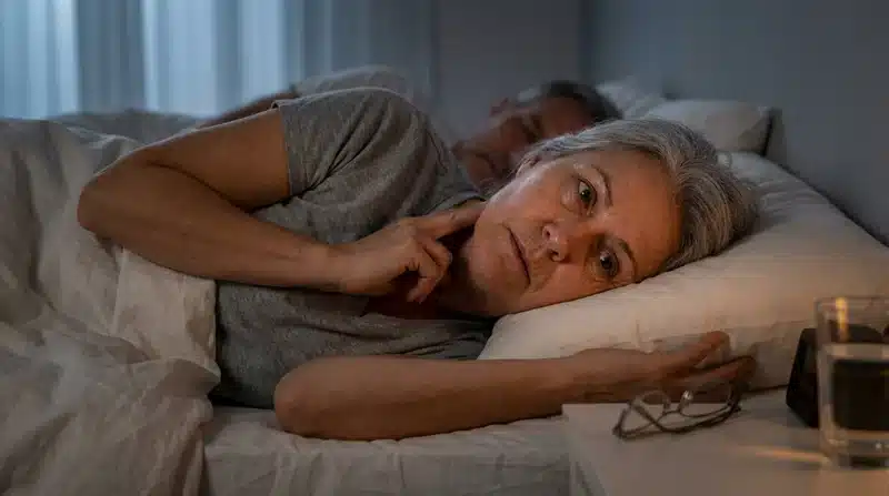 Frau liegt nachts wach im Bett auf der rechten Seite, Hand am Hals, prüft den Puls