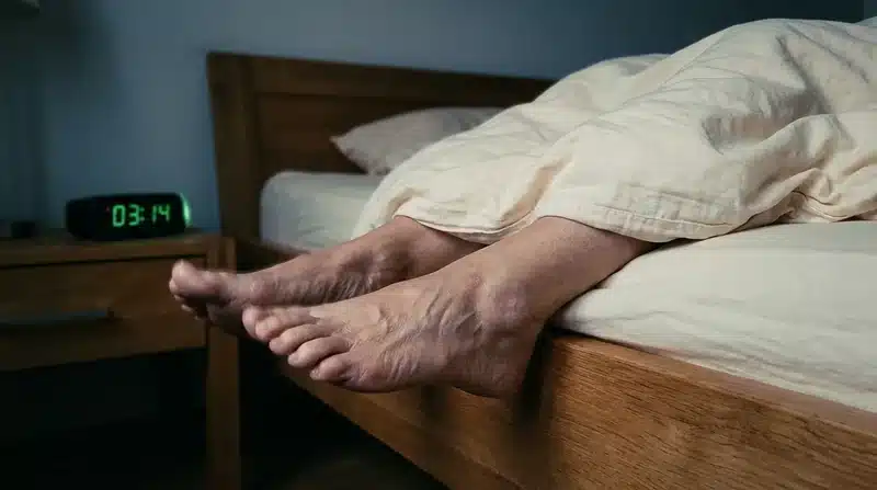 Nackte Füße hängen nachts über die Bettkante — nur das grüne Licht des Weckers leuchtet
